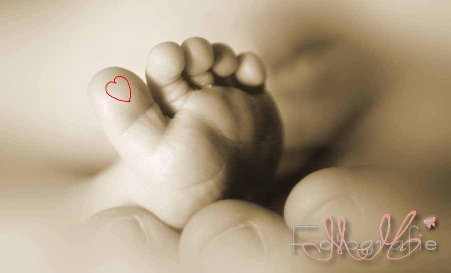 Schöne Sepia-Fotografie eines Babyfüßchens. Auf der großen Zehe ist ein kleines rotes Herz aufgemalt