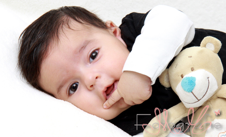 Babyfoto eines kleinen Jungen, der mit großen Augen verschmitzt in die Kamera schaut.