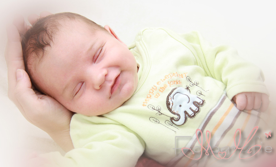Selig lächelnd liegt das Baby in den Händen seines Vaters.