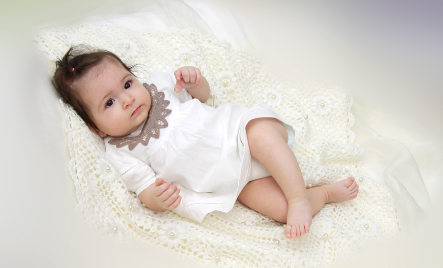 Babyfoto eines kleinen Mädchens, sechs Monate altes Baby, liegt auf dem Rücken auf einer Häkeldecke.