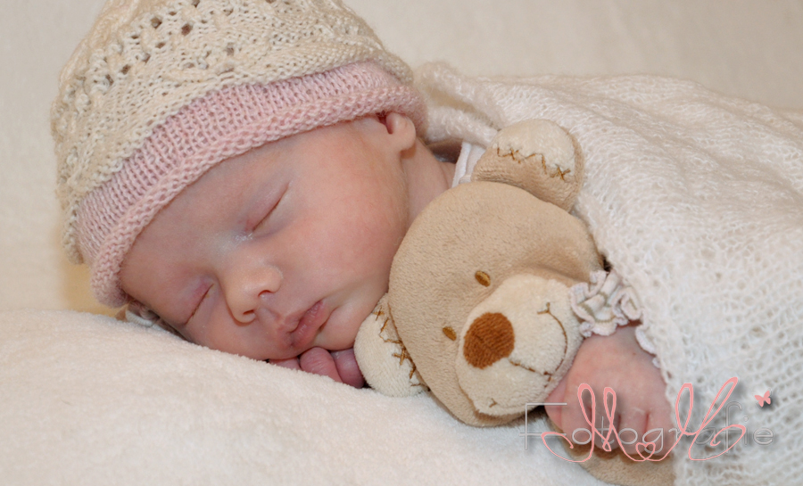Kleines neugeborenes Baby auf dem Bauch liegend mit Teddy im Arm