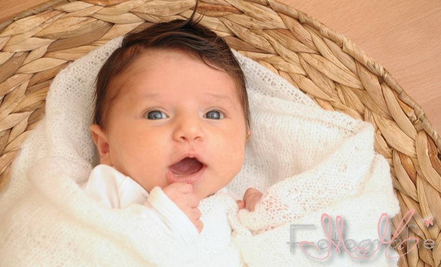Portrait eines ganz kleinen Babys, in einem Körbchen, lächelnd.