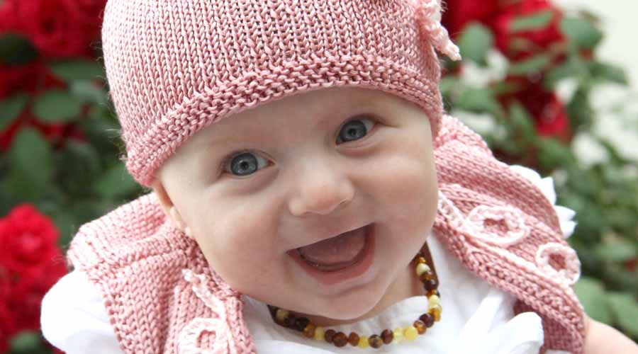 Laura lacht und strahlt in die Kamera - sie hat ihr süßes rosa Mützchen auf und eine passende kleine Weste an