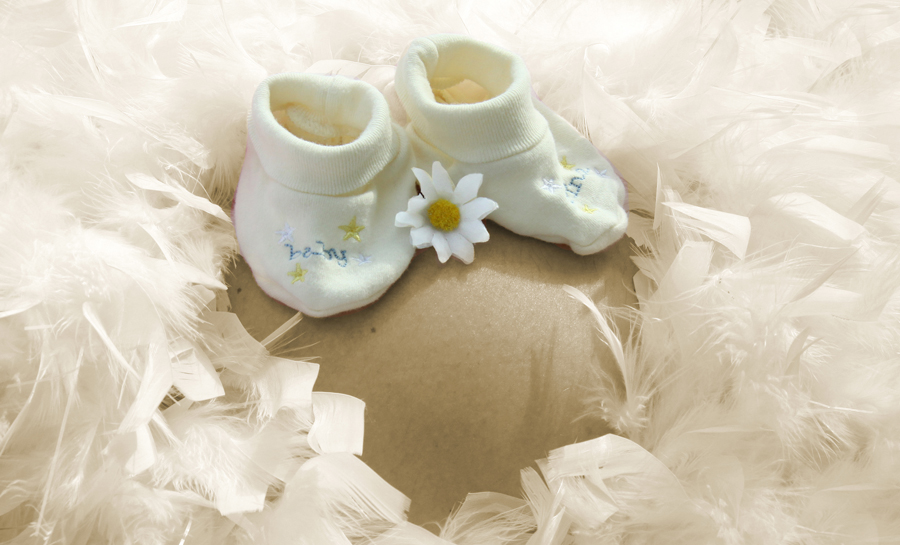 Federboa auf dem Bauch mit Babyschuhen und Blümchen