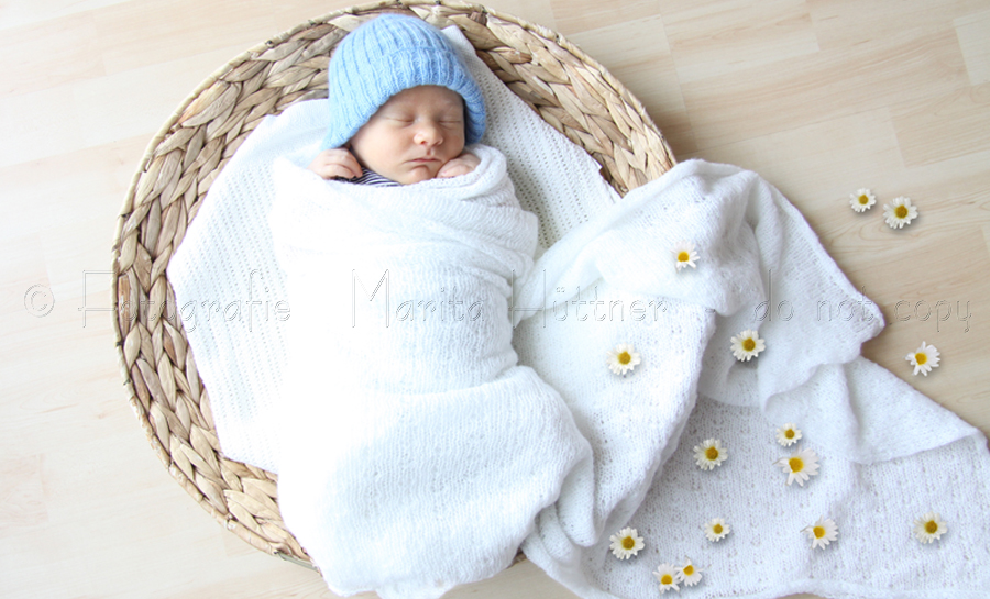 Ein kleines Baby mit blauem Mützchen liegt in einem runden Körbchen