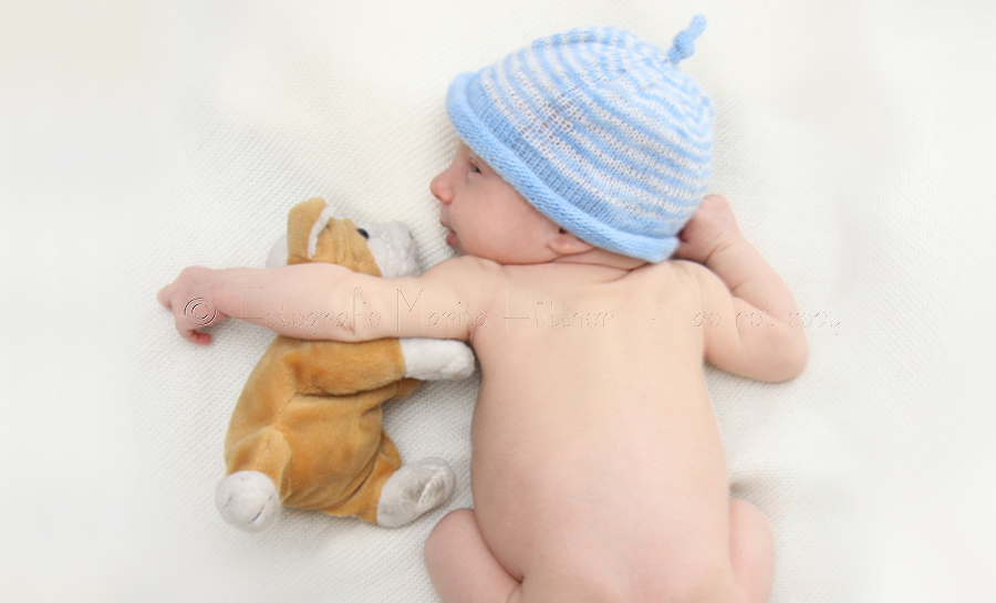 neugeborener Junge mit Mützchen und Kuscheltier