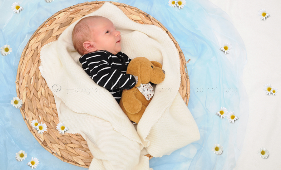 kleines Baby in einem Korb - der Untergrund ist eine blaue Decke auf der Blümchen liegen